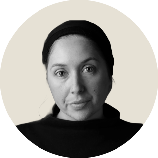 Black and white portrait of a woman wearing a dark top and headband, looking at camera.